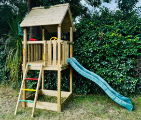 Compact wooden playhouse with green slide and climbing ladder next to a hedge