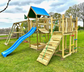 Large wooden climbing frame with slide, climbing wall and wobble bridge on a lawn